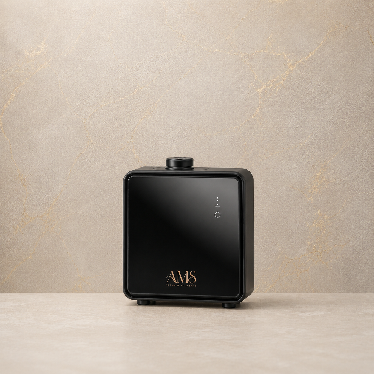 A black square electronic diffuser with rounded corners, featuring a glossy front panel, gold 'AMS' branding, and small white power icons, set on a light beige surface against a textured beige background.