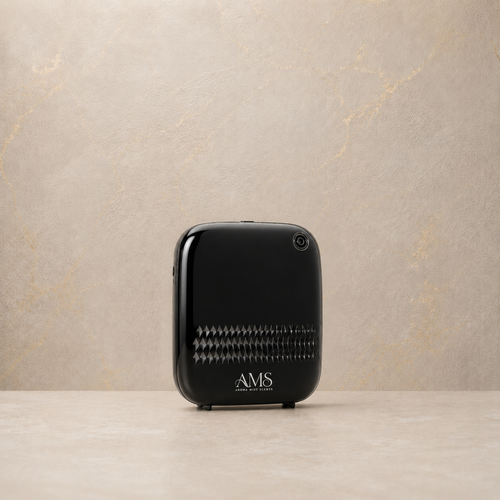A black AMS diffuser with a glossy finish and a textured front grille, standing on a light beige surface against a textured beige wall.