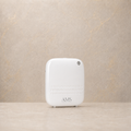 A white diffuser with the brand name 'AMS' printed on the front, standing on a light beige surface against a textured beige wall.
