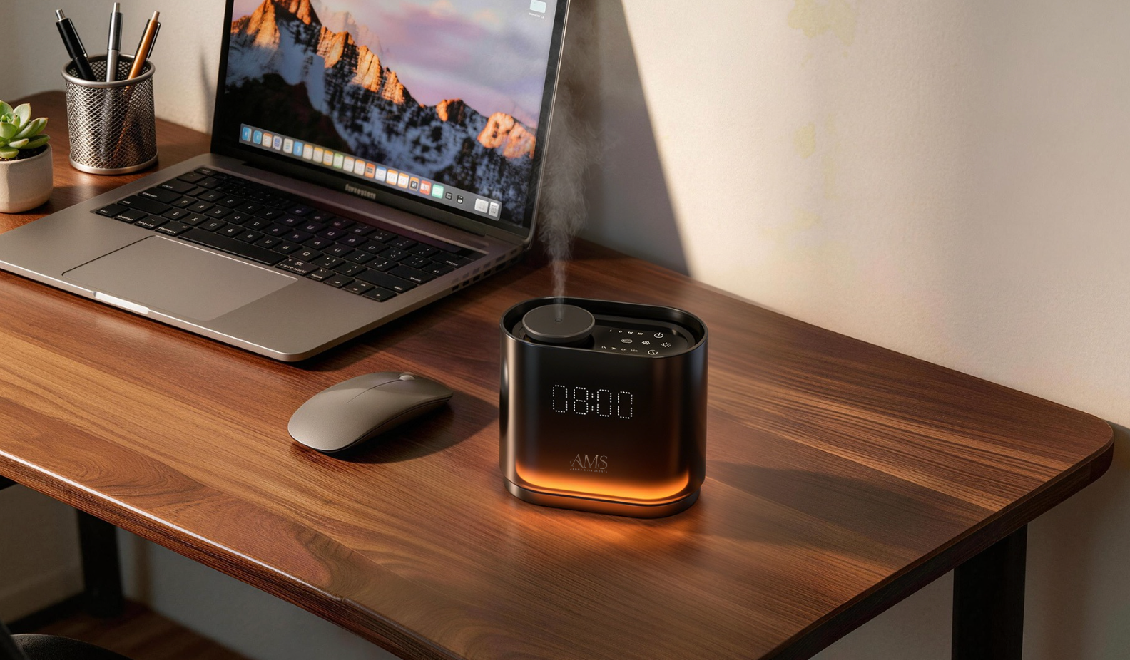 A black ams diffuser with a glowing amber base sits on a wooden desk next to a laptop and mouse, emitting a visible steam cloud.