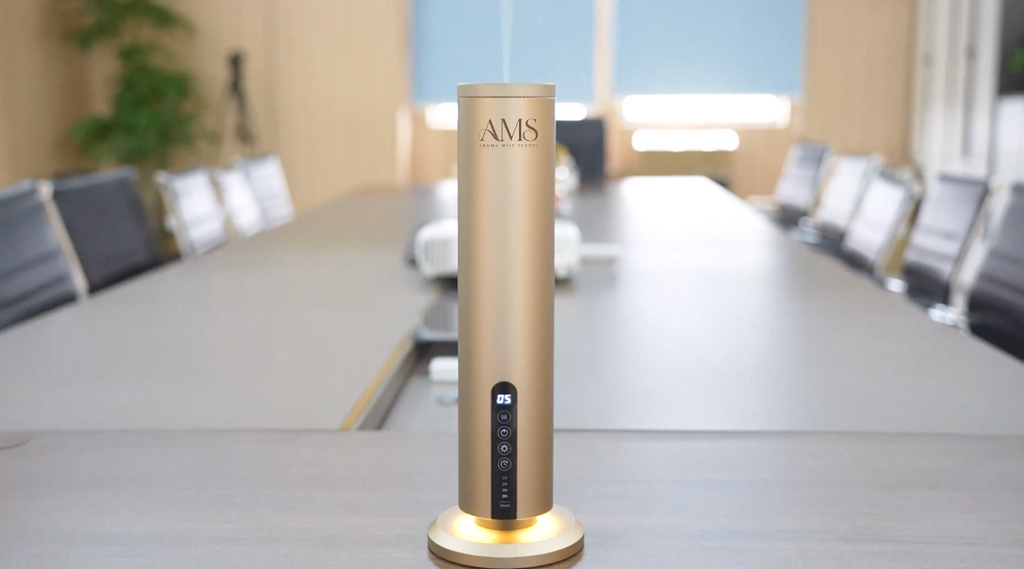 A sleek, cylindrical gold diffuser with a metallic finish and a small black control panel, standing on a matching gold base on a conference table in a modern office setting.