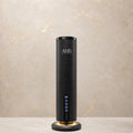 A sleek black cylindrical AMS diffuser with a glowing circular base, standing on a light stone surface against a textured beige wall.
