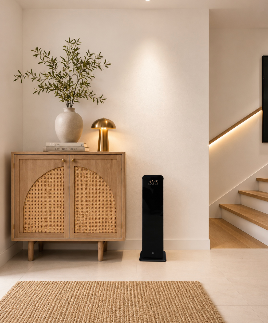 A modern interior scene featuring a tall black floor-standing diffuser next to a light wood cabinet with woven cane doors, styled with a white vase of greenery and a gold table lamp.