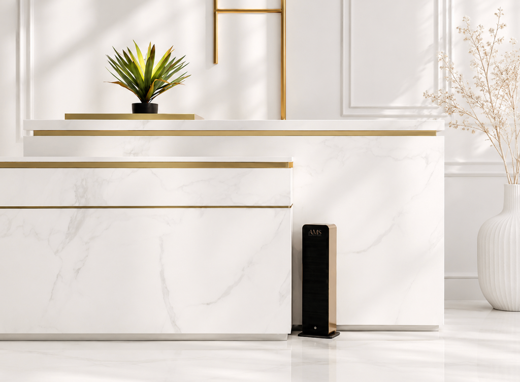 A modern white marble-look cabinet with gold metal trim, shown in a bright interior setting with a small potted plant on top and a black floor diffuser beside it.